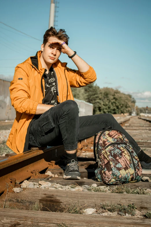 a man sitting on a train track with a backpack, a portrait, trending on pexels, graffiti, patterned clothing, avatar image, brown, full product shot