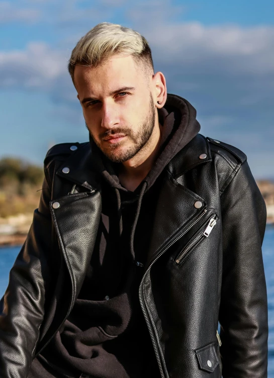 a man in black jacket near water with his hair flying back