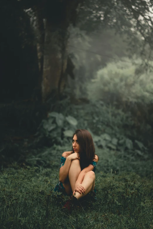 a woman crouching in the middle of a forest