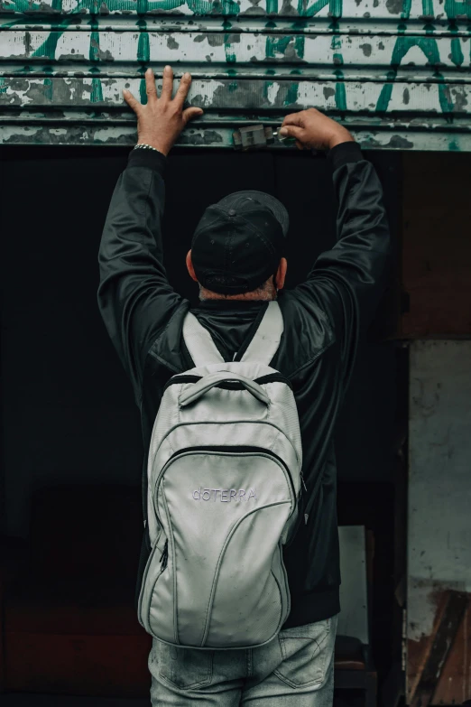 a man with a backpack standing in front of a building, grey and silver, trending on r/streetwear, arched back, off white