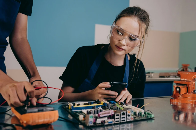 a young girl is working on an electronic device, by Lee Loughridge, pexels, process art, teenage engineering moad, girl wearing uniform, very nerdy, thumbnail