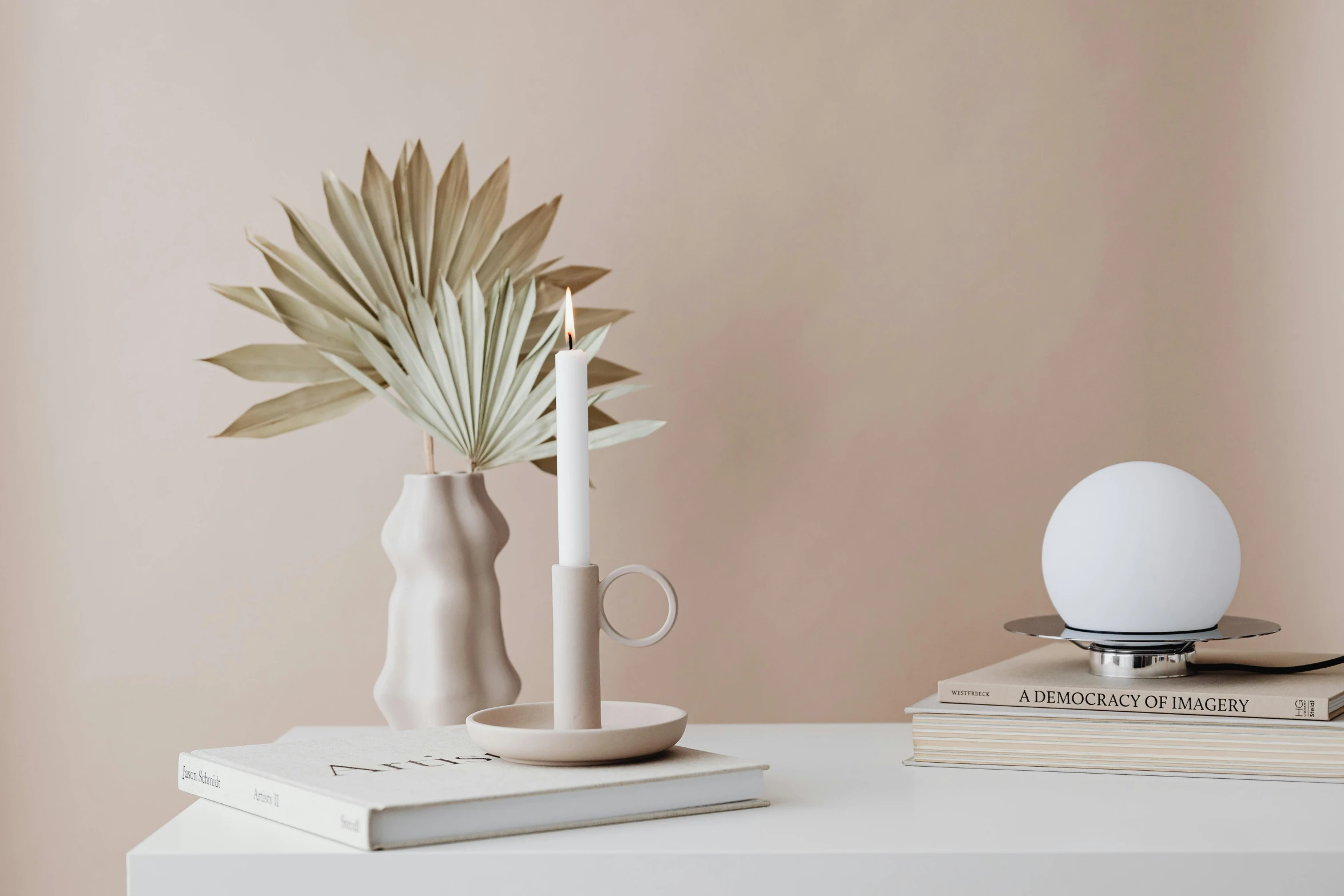 a white vase sitting on top of a table next to a stack of books, a still life, featured on pinterest, minimalism, holding a candle holder, earthy light pastel colours, palme d'or winner, flat neutral tone