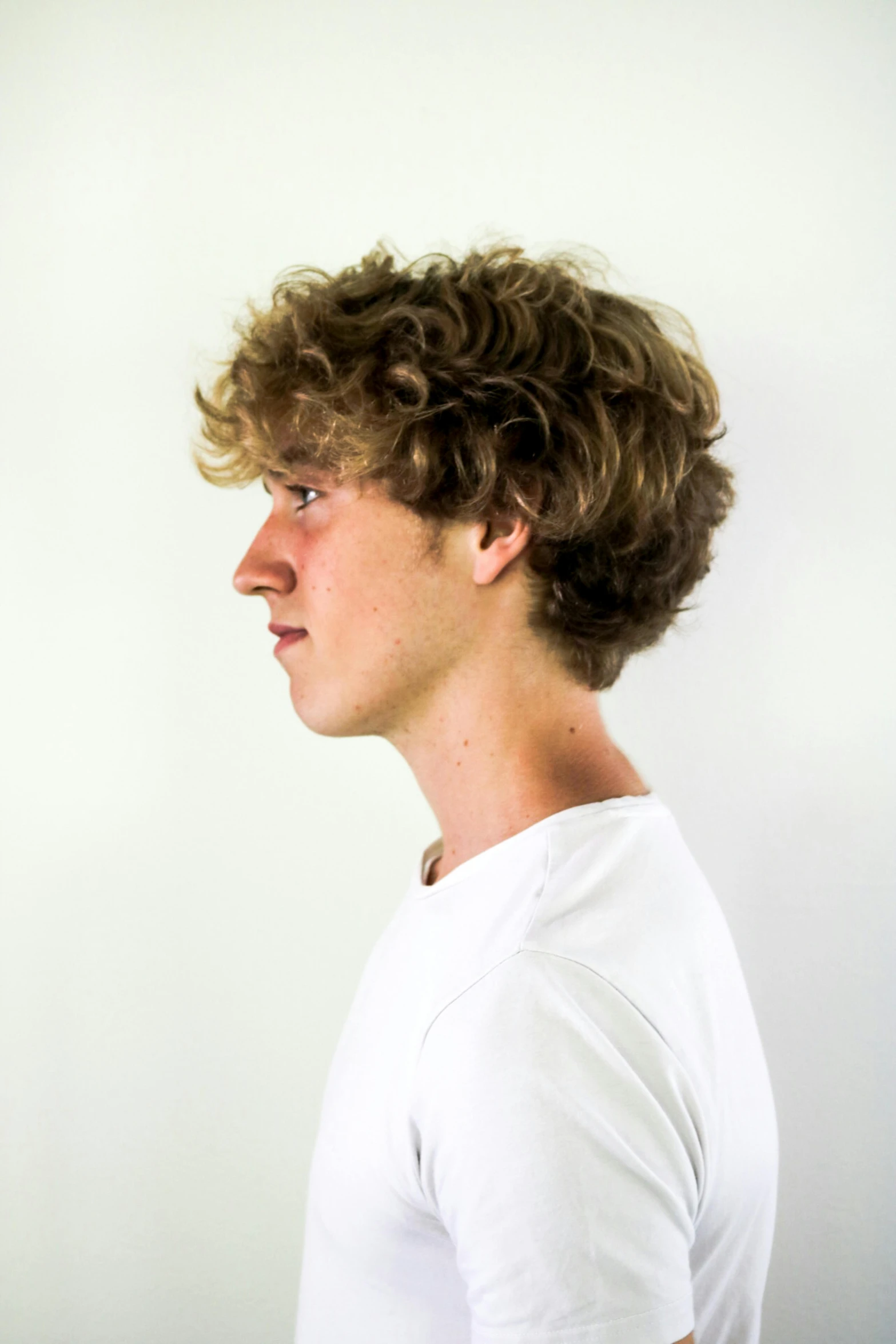 a young man standing in front of a white wall, an album cover, by Jacob Toorenvliet, pexels contest winner, renaissance, very very curly blond hair, profile image, discord profile picture, acting headshot