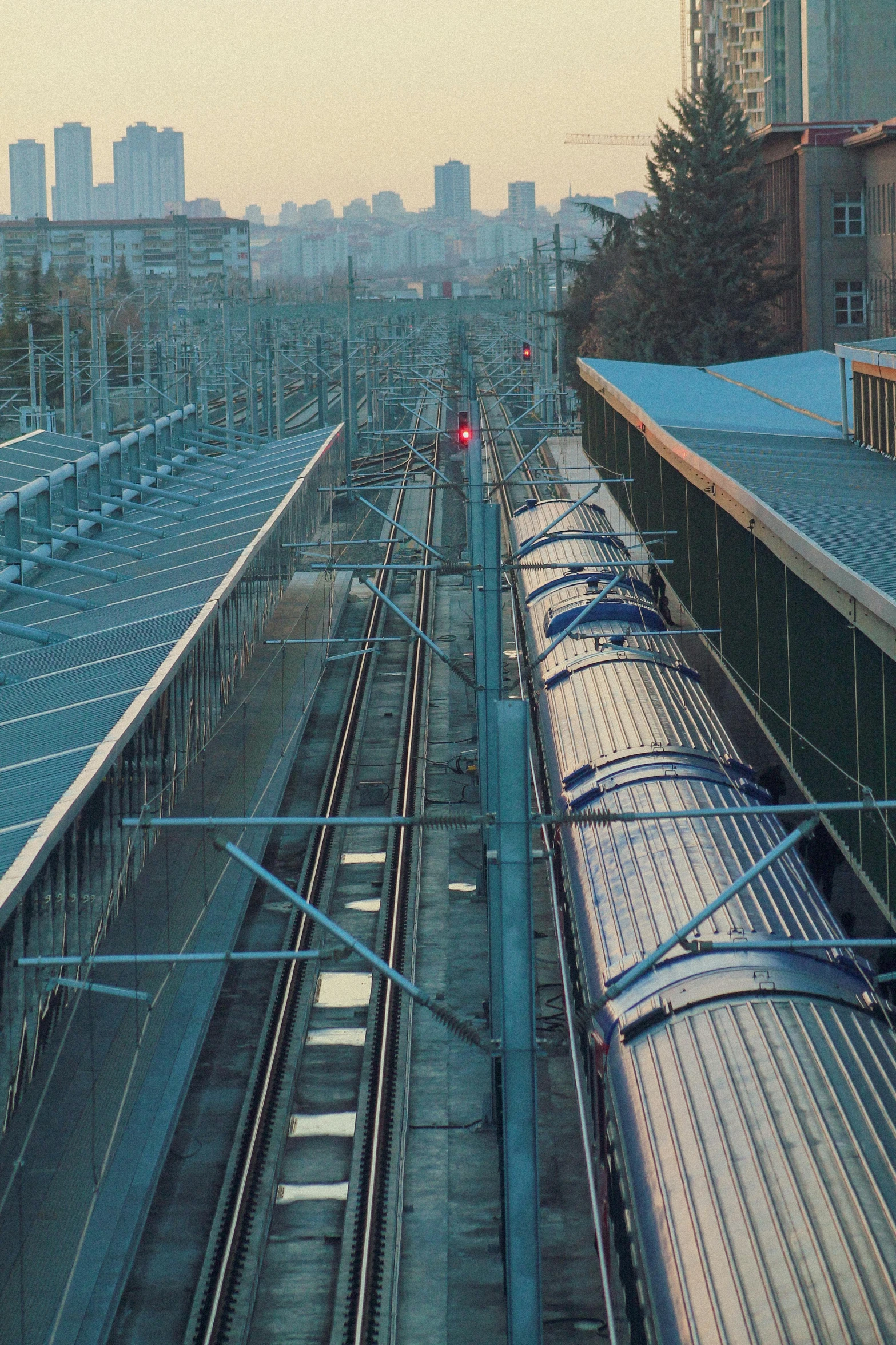 a train traveling down train tracks next to tall buildings, tubes and cables, soft lighting from above, transmitters on roof, large pipes