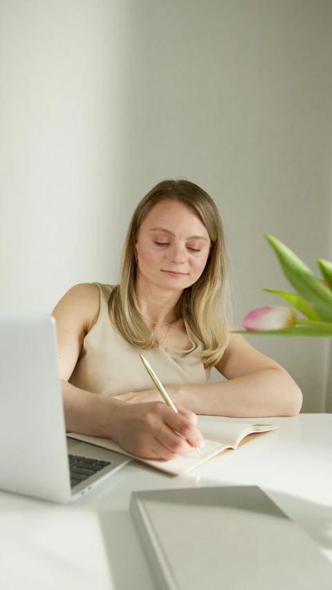 a woman sitting at a table in front of a laptop, writing in journal, blonde swedish woman, thumbnail, low quality photo