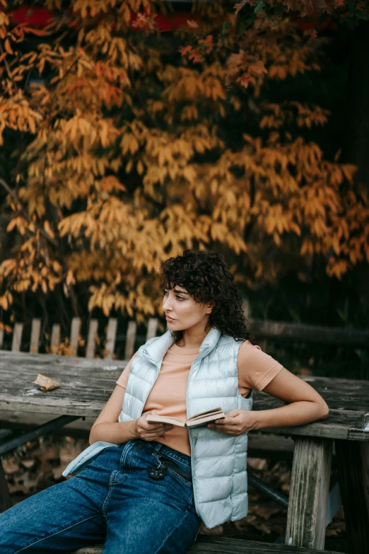 a woman sitting on a bench reading a book, a portrait, pexels contest winner, happening, muted fall colors, sydney park, curls, handsome girl