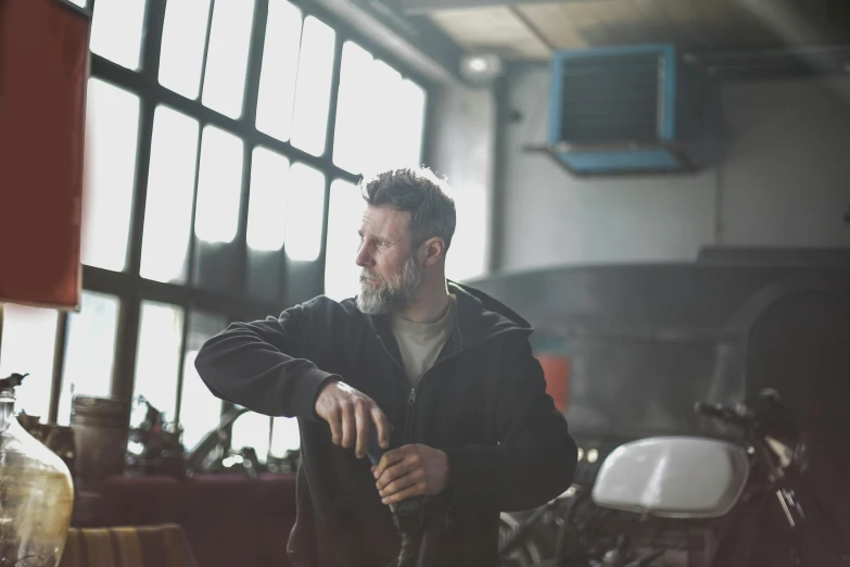 a man standing next to a motorcycle in a garage, by John Murdoch, pexels contest winner, holding a wrench, gray men, pondering, bearded and built