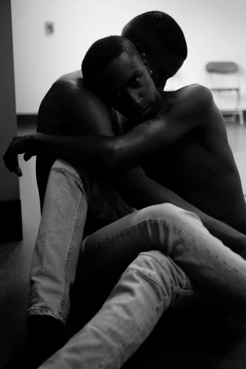 a couple of people sitting next to each other, a black and white photo, by Clifford Ross, adut akech, hugging his knees, man is with black skin, dim moody lighting