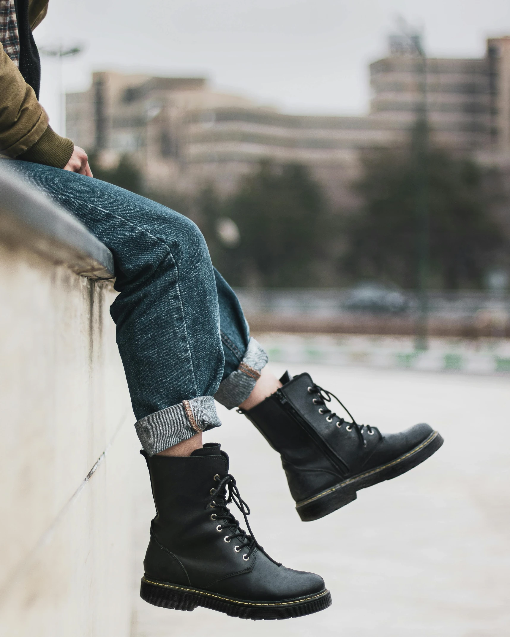 a person wearing black boots and jeans sitting on a wall