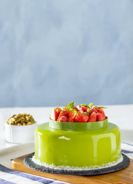 a green cake sitting on top of a wooden cutting board, a pastel, inspired by François Louis Thomas Francia, next to sliced strawberries, ultra glossy, ceramic base, jelly glow