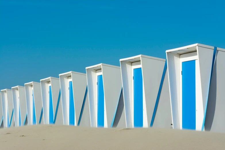 a row of beach huts sitting on top of a sandy beach, a photo, inspired by Ricardo Bofill, pexels contest winner, conceptual art, white panels, blue, toilet, futuristic france