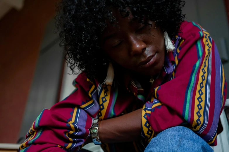 a woman sitting on the steps of a house, an album cover, by Lily Delissa Joseph, trending on pexels, hurufiyya, wearing a colorful coogi sweater, depressed sad expression, east african man with curly hair, moody dim lighting