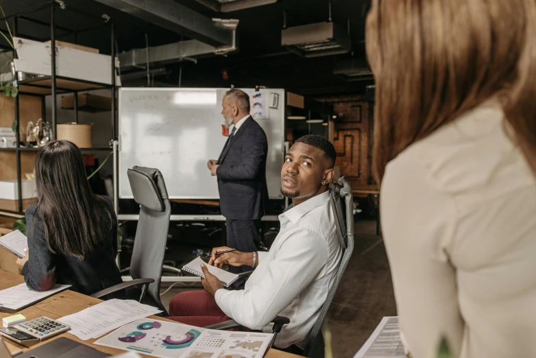 a group of people sitting around a wooden table, trending on unsplash, whiteboards, background image, man sitting facing away, stacked image