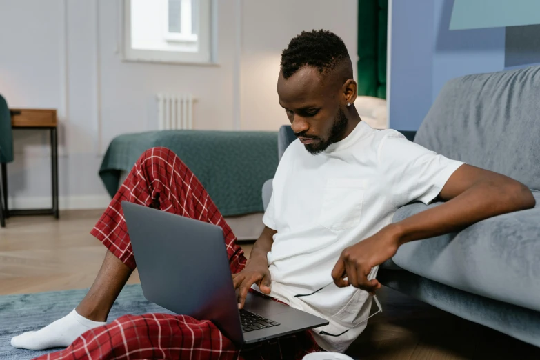 a man sitting on the floor using a laptop, trending on pexels, happening, african aaron paul, someone in home sits in bed, sitting on a red button, unmistakably kenyan