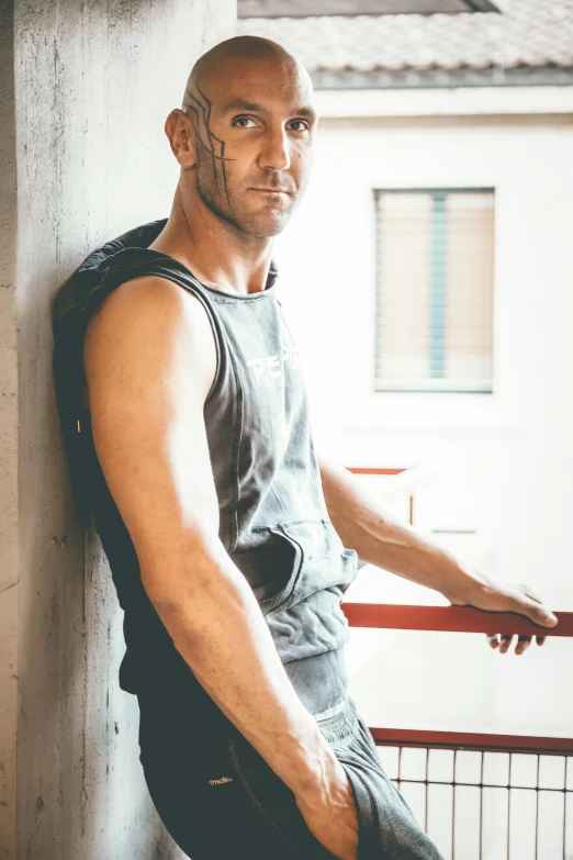 a man in a tank top leaning against a wall, a photo, trending on pexels, jason statham, vests and corsets, postprocessed), fit pic