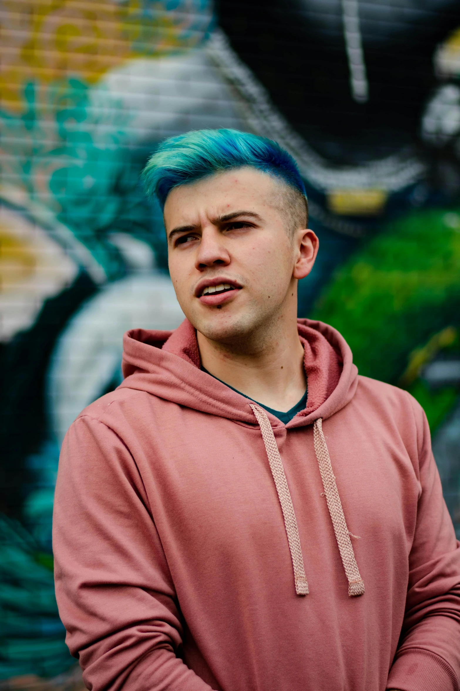 a man with blue hair standing in front of a graffiti wall, featured on reddit, caspar david, headshot profile picture, with teal clothes, proud looking away