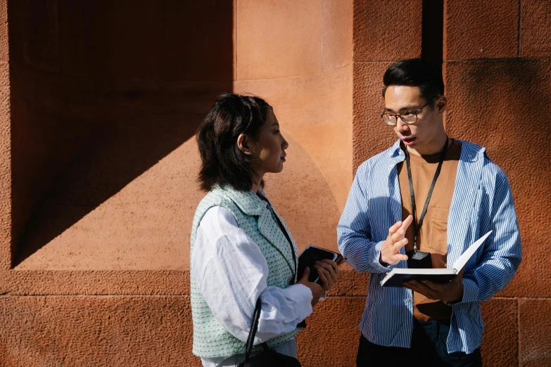 a man and a woman standing next to each other, pexels contest winner, academic art, holding notebook, darren quach, talking, in the sun