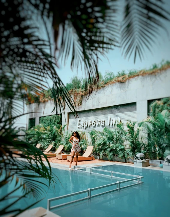 a woman posing in front of a large pool with lounge chairs