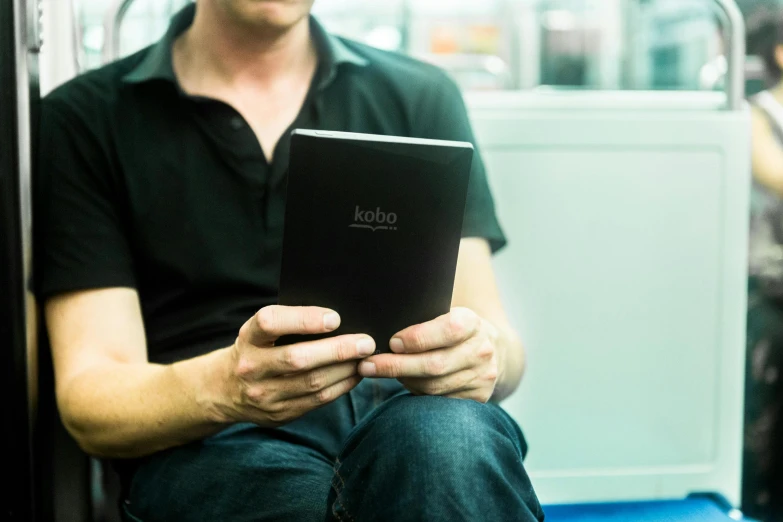 a man sitting on a bus holding a tablet computer, an album cover, by Joe Bowler, reddit, figuration libre, closeup photograph, reading in library, robert kondo, with a long