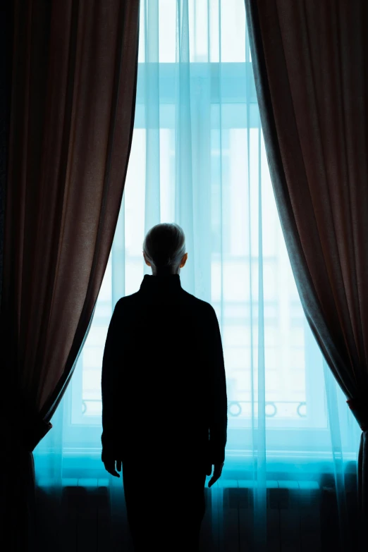 a person standing next to a window with a curtain open