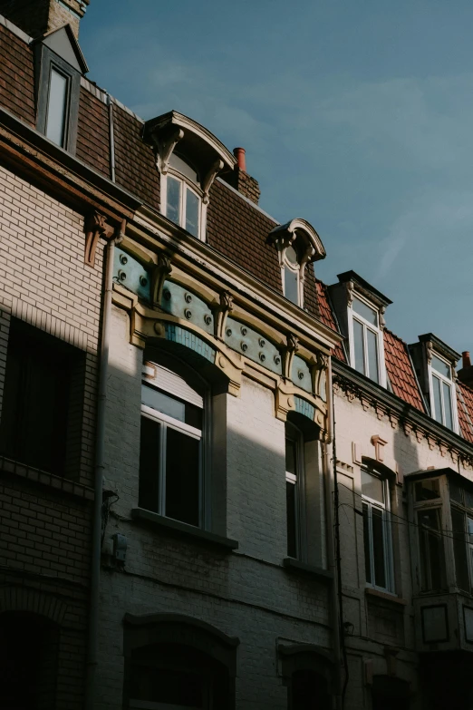 a clock that is on the side of a building, by Daniel Seghers, pexels contest winner, art nouveau, sunlight and whimsical houses, belgium, looking from slightly below, shady alleys