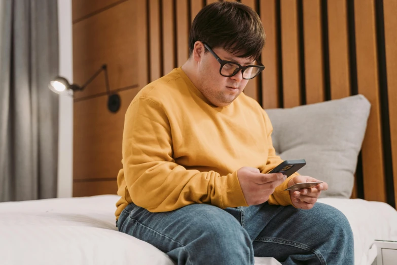 a man sitting on a bed looking at his cell phone, trending on pexels, pixel art, peter griffin body type, wearing a modern yellow tshirt, joel fletcher, bbwchan