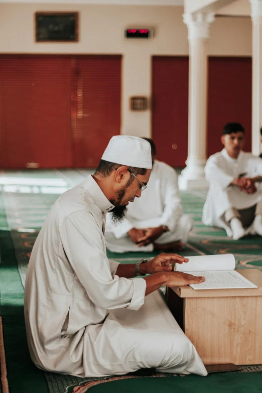 a group of men sitting on top of a green carpet, pexels contest winner, hurufiyya, writing a letter, he is in a mosque, wearing white cloths, post graduate