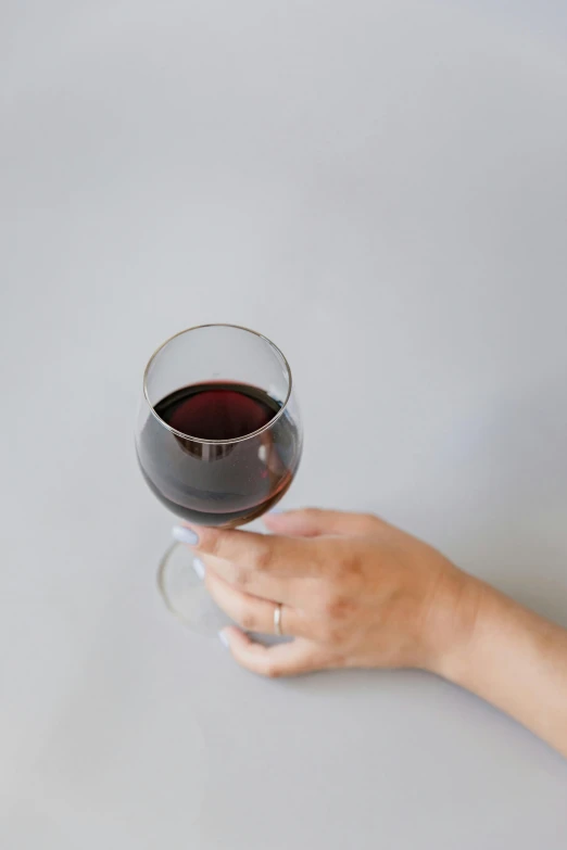 a hand holds a wine glass with red wine