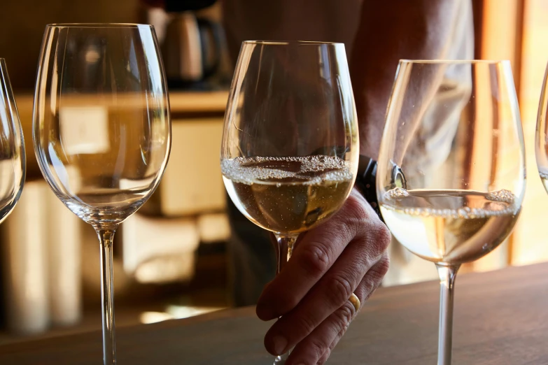 a person's hand is holding on to the rim of five wine glasses