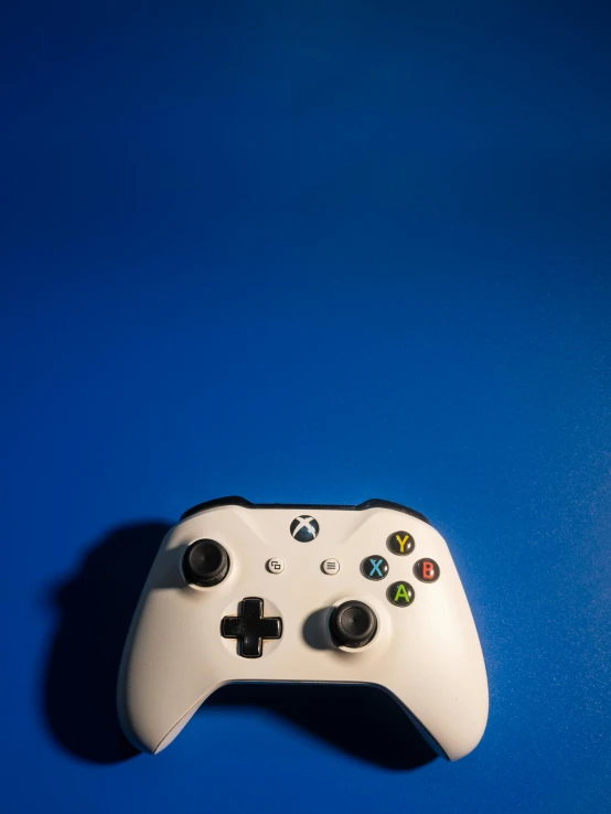 a white controller sitting on top of a blue surface, a portrait, by Carey Morris, unsplash, x - box, 15081959 21121991 01012000 4k