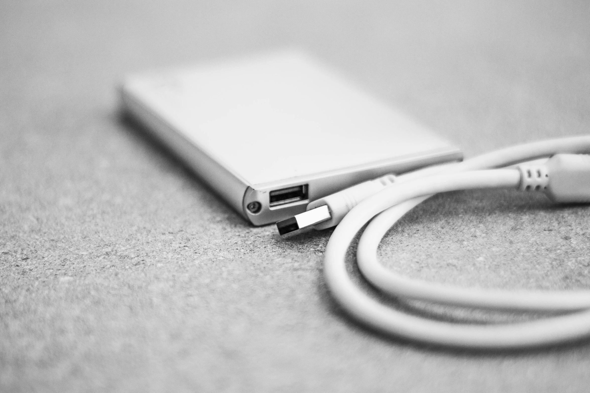 a cell phone sitting on top of a table next to a charger, a black and white photo, by Daniel Gelon, square, wire, closeup, soft white rubber