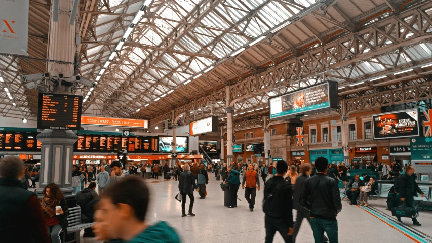 a group of people walking through a train station, teal and orange colours, london, 🚿🗝📝, very busy place