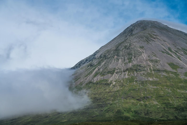 a tall mountain covered in grass and clouds