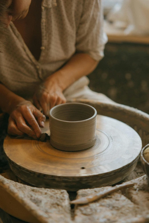 a woman is making a bowl out of clay, inspired by Hendrik Gerritsz Pot, trending on unsplash, on textured disc base, with a white mug, historical setting, sydney hanson