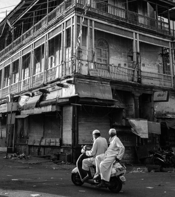 a couple of people riding a motorcycle down a street, a black and white photo, “derelict architecture buildings, in sci - fi mumbai, chaotic riots in 2022, paisley