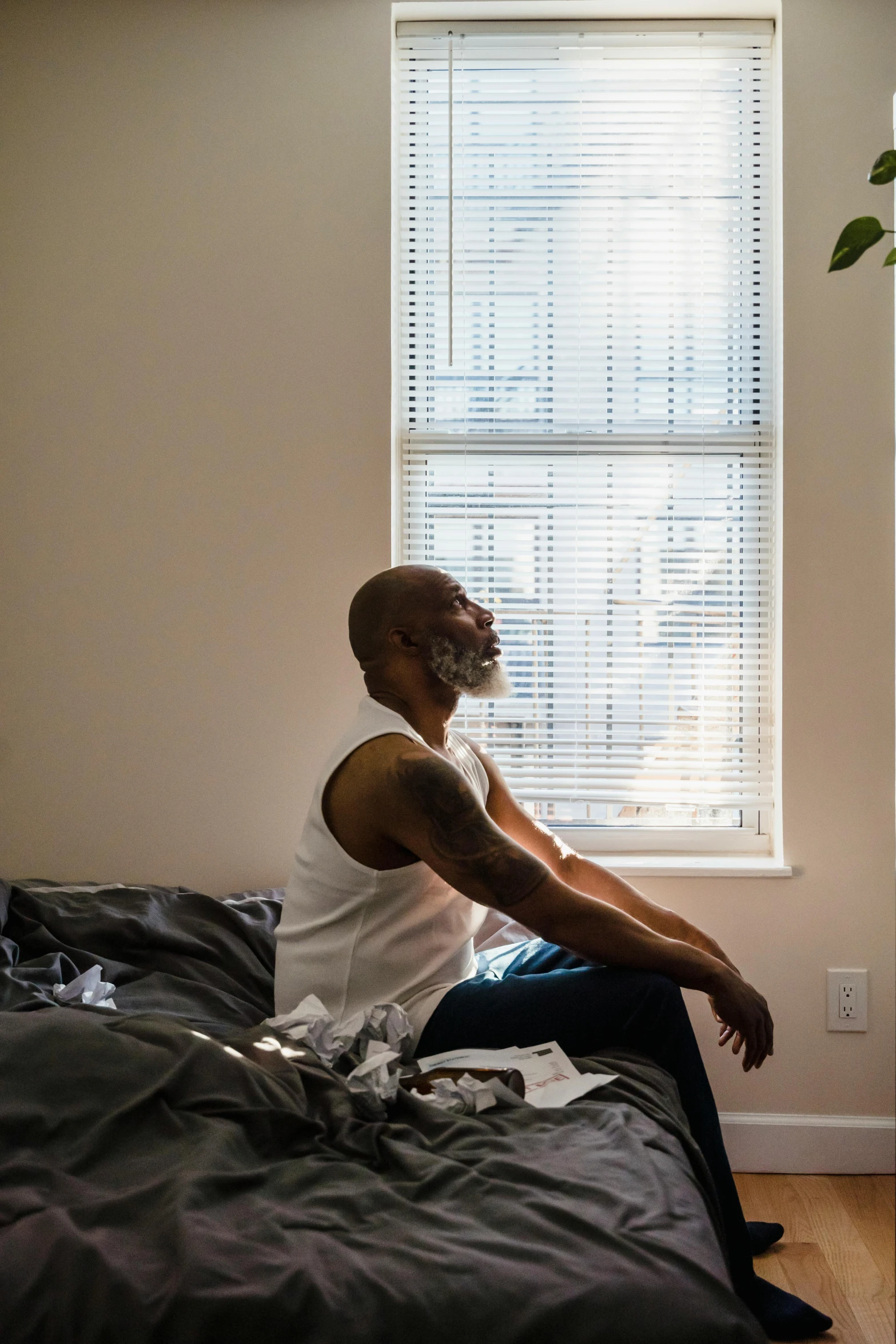 a man sitting on the edge of a bed in front of a window