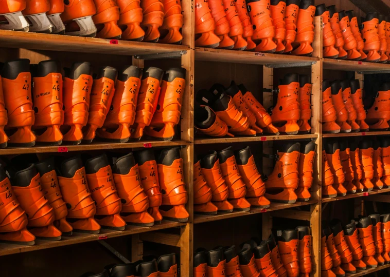 a room filled with lots of orange shoes, prosthetic limbs, full ice hockey goalie gear, worksafe. instagram photo, kneehigh boots