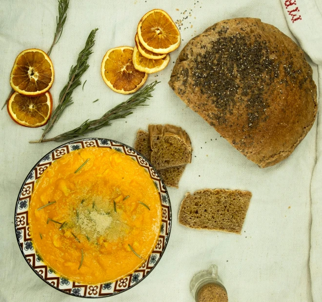 a table topped with a bowl of soup next to slices of bread, inspired by Géza Dósa, orange minerals, high quality product image”