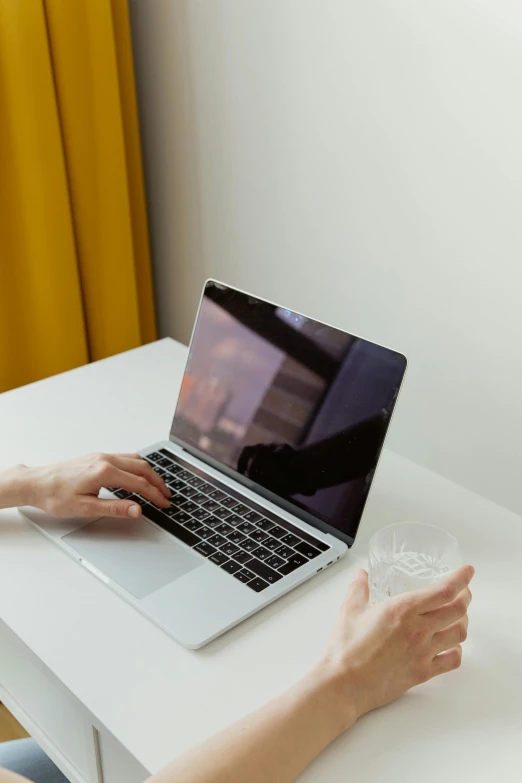 a woman sitting at a table using a laptop computer, by Carey Morris, pexels, holding a drink, minimalist home office, close up to the screen, awarding winning