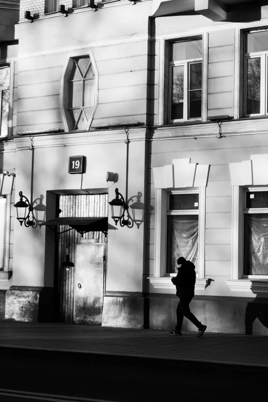 a black and white photo of a person walking in front of a building, typical russian atmosphere, square, 8k 50mm iso 10, buildings