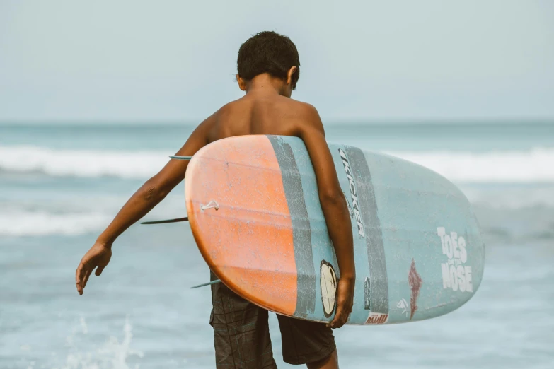 a young boy carrying a surfboard into the ocean, pexels contest winner, black teenage boy, background image, english, detailed information