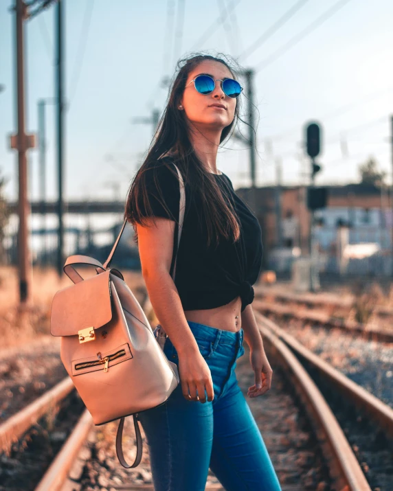 a woman standing on a train track with a backpack, trending on pexels, wearing shades, bisexual lighting, instagram picture, tan complexion