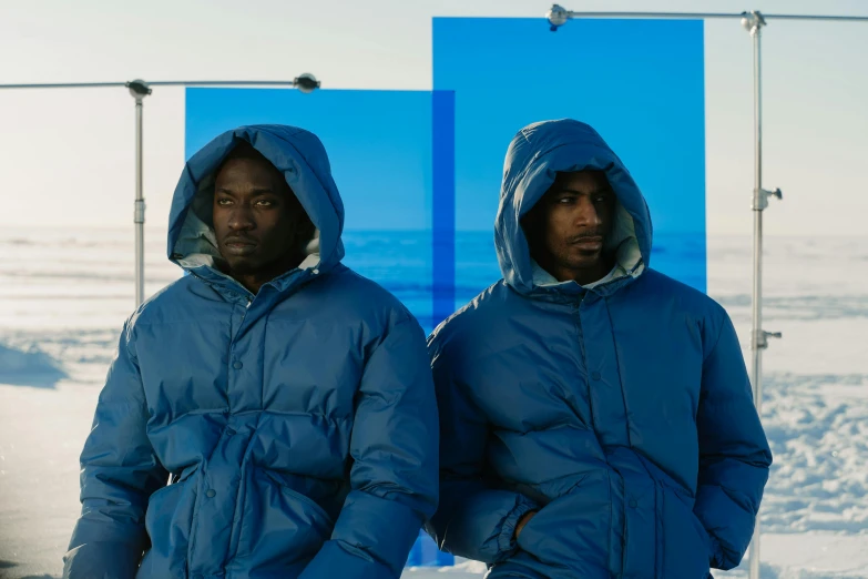 two men standing in the snow wearing blue jackets