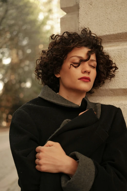 a woman leaning against a wall with her eyes closed, an album cover, curly and short top hair, roma, wearing a turtleneck and jacket, dark. no text