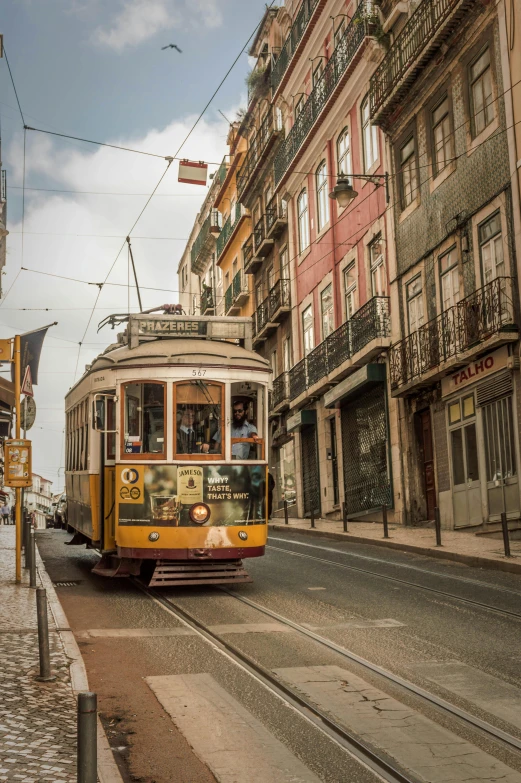 a yellow trolley traveling down a street next to tall buildings, a picture, inspired by Almada Negreiros, pexels contest winner, renaissance, sepia colors, square, baroque winding cobbled streets, mies van der rohe