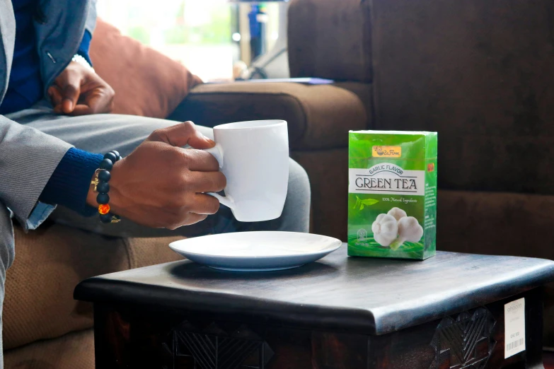 a man sitting on a couch holding a cup of coffee, inspired by Johan Grenier, happening, assam tea garden setting, vibrant green, official product image, ready to eat