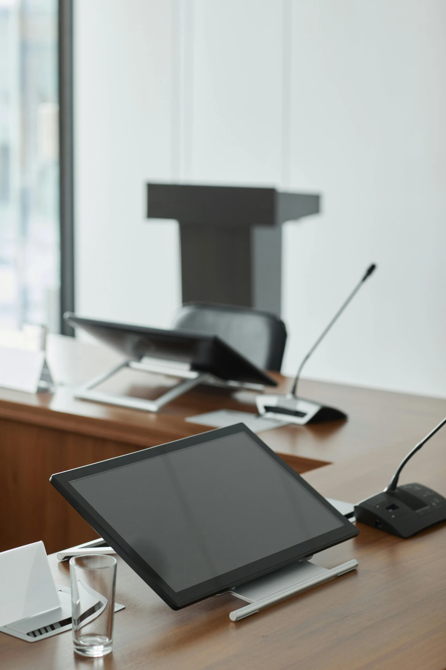 a laptop computer sitting on top of a wooden desk, witness stand, table with microphones, in a meeting room, black wired cables