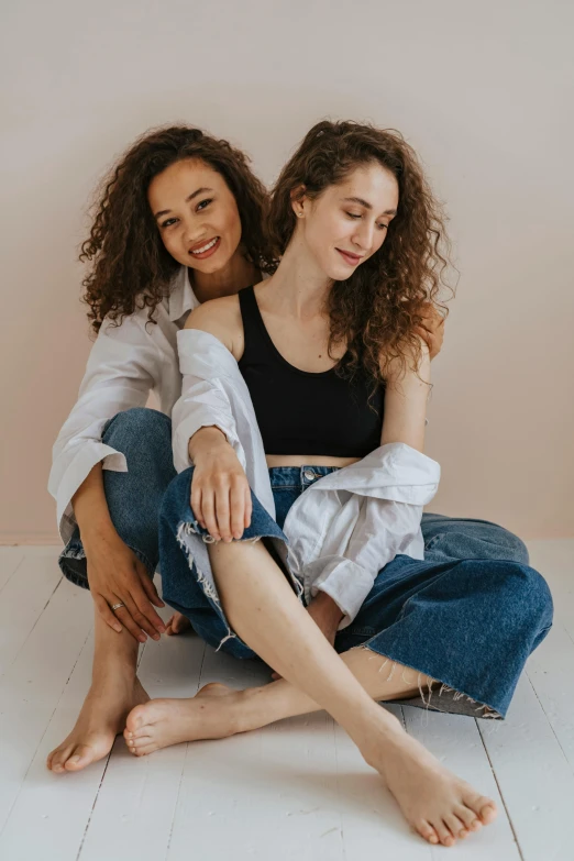 two women sitting on the floor next to each other, trending on pexels, renaissance, curly brown hair, arm around her neck, denim, lesbian