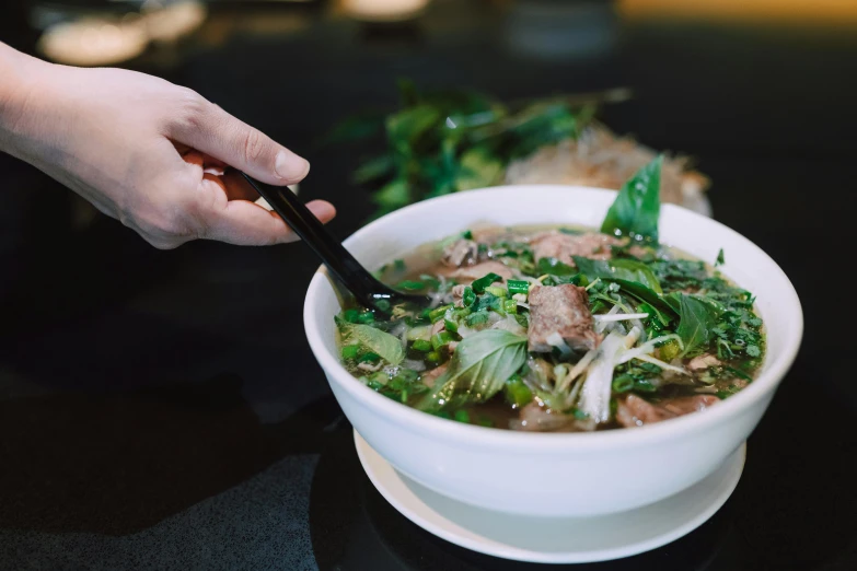 someone eating soup on a table with green vegetables