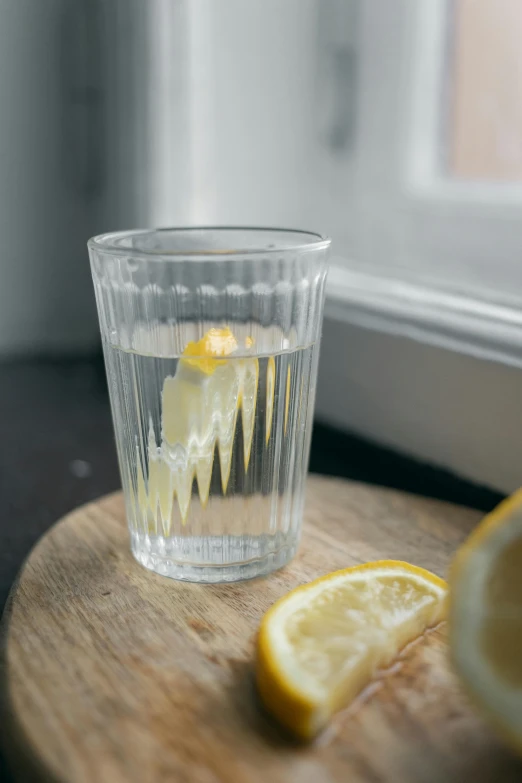 a glass of water sitting on top of a wooden cutting board, lemon, a pair of ribbed, subtle detailing, lifestyle